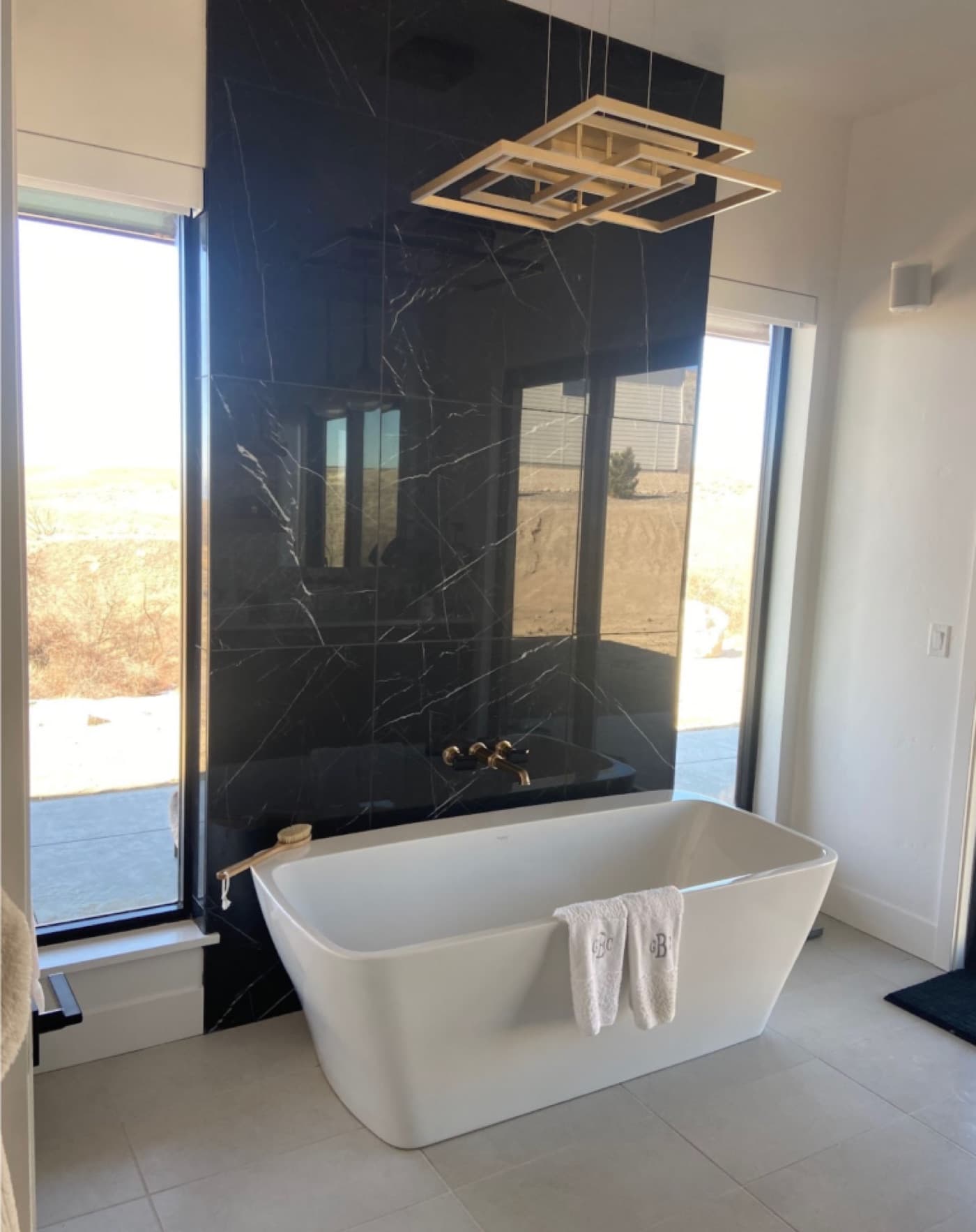 Freestanding soaking tub with wall-mounted filler against a black marble surround