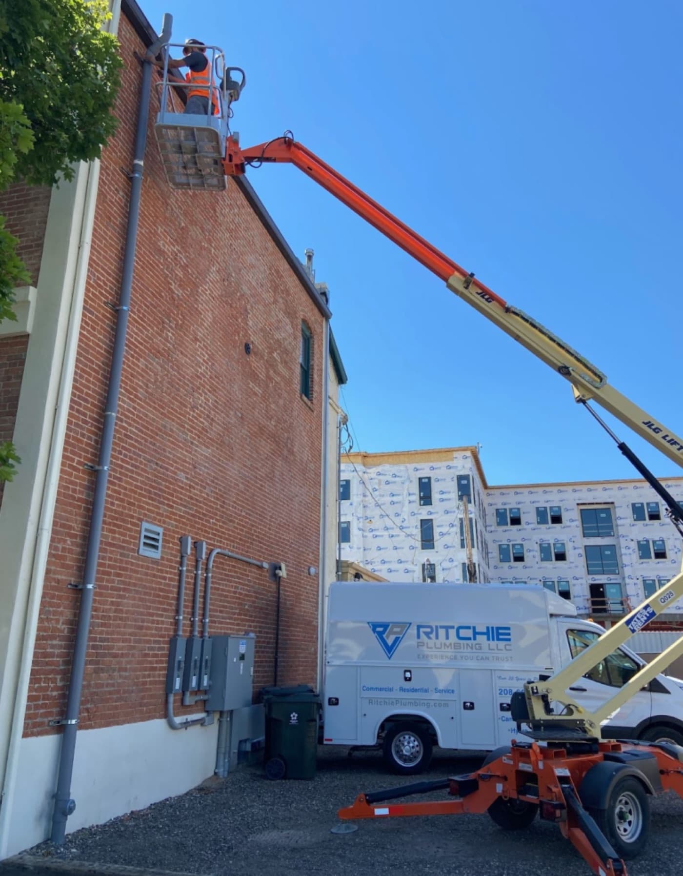 Technician on a boom lift servicing plumbing on a brick commercial building
