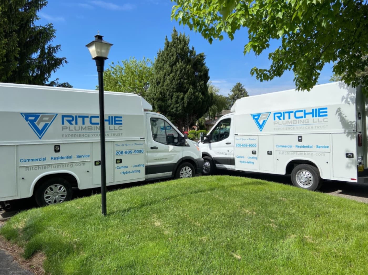 Two Ritchie Plumbing vans parked on a tree-lined Boise street