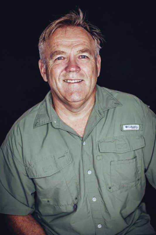 A smiling, congenial plumber - Mr. Ritchie. He wears a green button-up shirt; his greying hair short and professional.