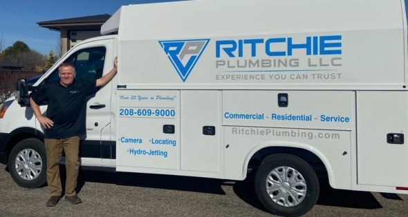 Ritchie, smiling, one hand on his hip, the other leaning against his work van. His company's logo is on the side of the van.